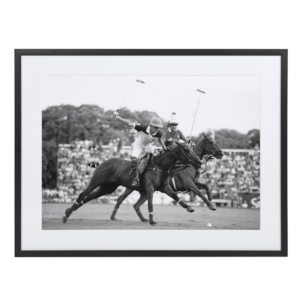 A stunning black and white snapshot capturing the dynamic energy of two polo players in action, racing across the field on their horses. The players, poised with mallets raised, are framed against a backdrop of an eager crowd, evoking the excitement and grace of the game. The photograph measures 66 x 86 cm and is elegantly set in a passe-partout, making it a timeless piece that brings a sense of movement and sophistication to any space.